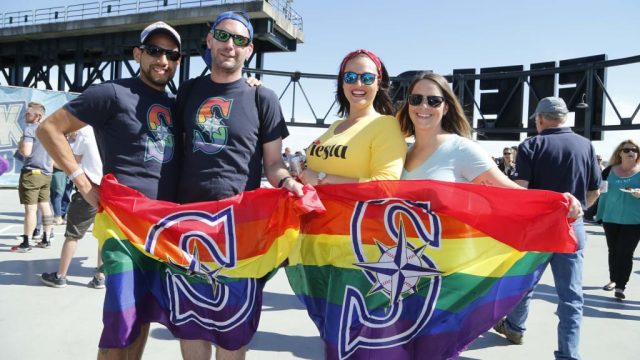 event-mariners-pride-night Seattle Mariners fans hold rainbow Pride flags with the Mariners logo