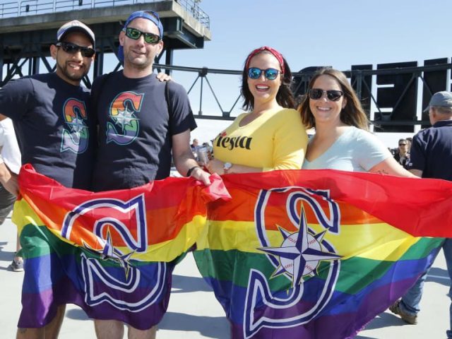 Seattle Mariners fans hold rainbow Pride flags with the Mariners logo
