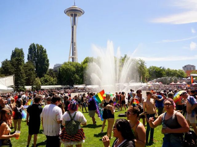 People hold rainbow Pride flags at Seattle Center in front of the Space Needle